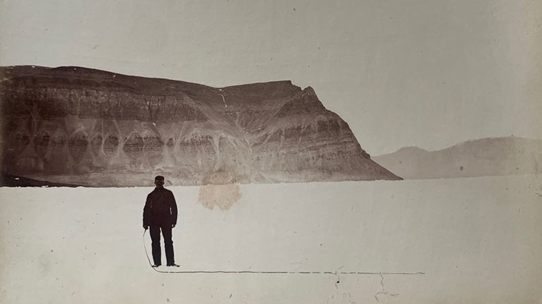 A portrait of a man with mountains behind him, gazing toward the camera.